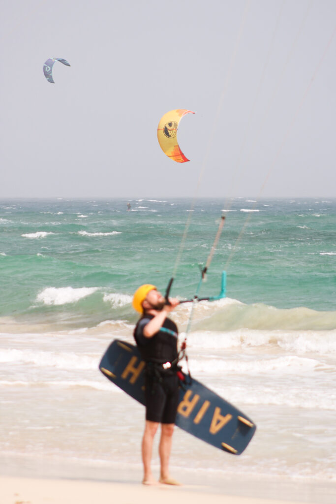 Kite surfer ready to get in to the turquoise waters at kite beach at the island Sal in Cabo Verde with a yellow kite in the background