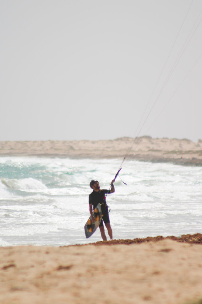 Kite surfer getting out of the water with a landscape of sand dunes in the background, learn how to kite at kite beach on the island of Sal in Cabo Verde